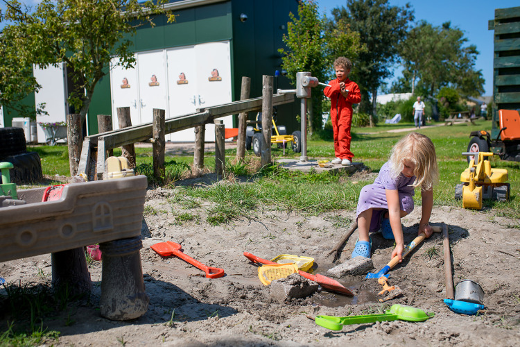 Kinder spielen im Sandkasten mit Spielzeug auf dem FarmCamps Fleur Stables Ferienpark in Nordholland.