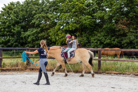 Niños montando a caballo bajo supervisión en FarmCamps Fleur Stables, un parque de vacaciones en Holanda.