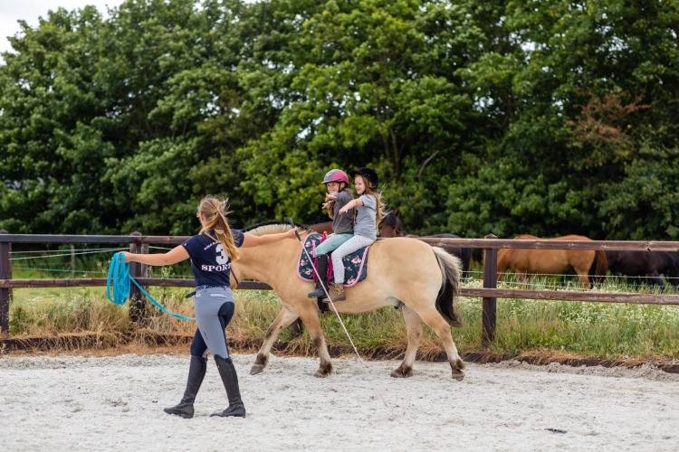 Kinder reiten unter Aufsicht einer Lehrerin auf einem Pferd bei FarmCamps Fleur Stables in Holland.