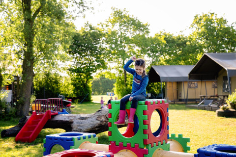 Ein Kind spielt auf bunten Spielblöcken auf dem Spielplatz bei FarmCamps Five Star in Zeeland, Niederlande.