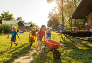 Kinder spielen mit Schubkarren im Freien auf dem FarmCamps Five Star Ferienpark in Zeeland, Niederlande.