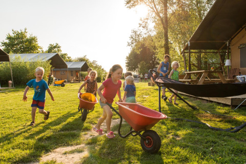 Kinder spielen mit Schubkarren im Freien auf dem FarmCamps Five Star Ferienpark in Zeeland, Niederlande.