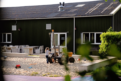 Child plays in sandbox at FarmCamps Five Star holiday park in Zeeland, Netherlands, with toys in sunlight.