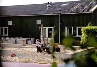 Child plays in sandbox at FarmCamps Five Star holiday park in Zeeland, Netherlands, with toys in sunlight.