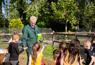 Kinderen luisteren naar een boer op FarmCamps Five Star vakantiepark in Zeeland, Nederland.