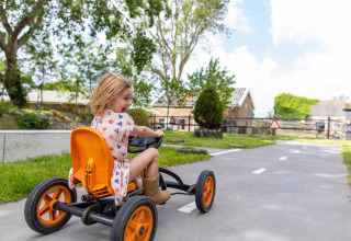 Un niño conduce un coche de pedales en un sendero pavimentado en FarmCamps Five Star, Zeeland, Países Bajos.
