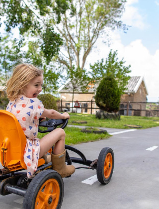 Ein Kind fährt ein Tretfahrzeug auf einem Weg bei FarmCamps Five Star in Zeeland, Niederlande.