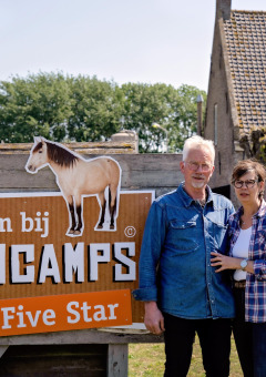Dos personas frente al cartel de FarmCamps Five Star en un parque vacacional rural en Zelanda, Países Bajos.