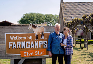Twee personen staan voor een FarmCamps Five Star-bord aan een vakantiehoeve in Zeeland, Nederland.