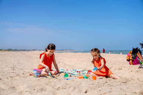 Dos niñas con vestidos naranjas juegan con cubos y palas en la playa de FarmCamps Five Star en Zeeland.