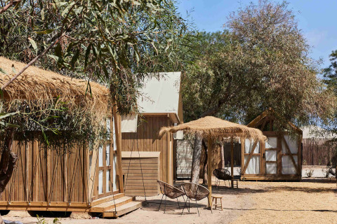 Außenbereich von TAIGA Almeria Playa mit Holzhütten, Strohdächern und Sitzgelegenheiten in Andalusien, Spanien.