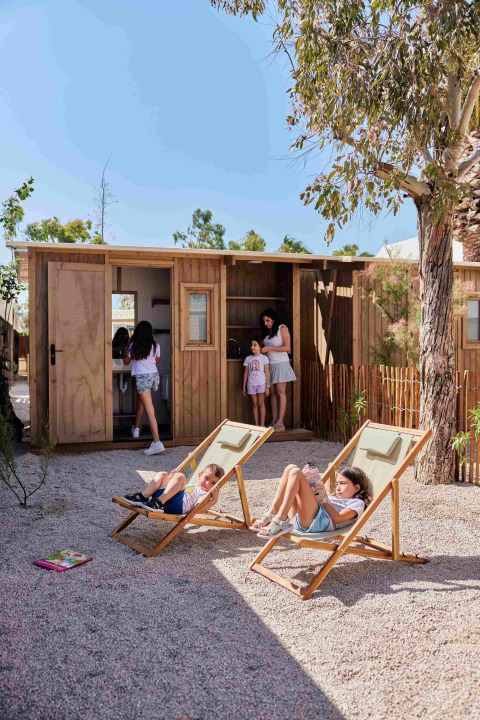 Kinder und Erwachsene entspannen vor Holzhütten im TAIGA Almeria Playa Ferienpark in Andalusien, Spanien.