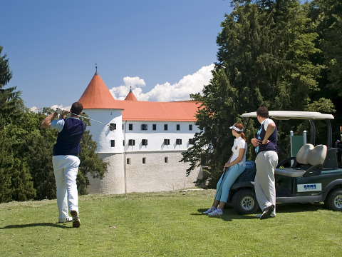 Persone che giocano a golf su un campo verde con vista castello al Camping Terme Catez in Slovenia.