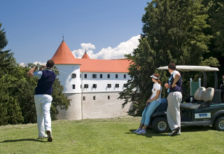Folk spiller golf ved en grøn bane med udsigt til et slot og træer på Camping Terme Catez i Slovenien.