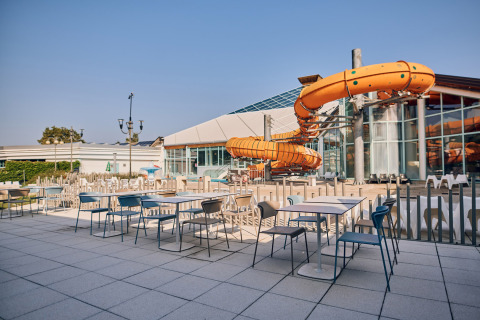 Outdoor dining area with tables and chairs next to a large orange water slide at Camping Terme Catez, Slovenia.
