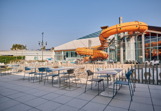 Außenterrasse mit Tischen und Stühlen neben einer großen orangefarbenen Wasserrutsche im Ferienpark Camping Terme Catez, Slowenien.