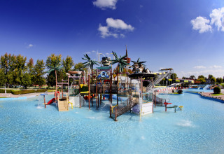 Wasserpark im Camping Terme Catez mit Wasserrutschen, Palmen und flachem Pool unter blauem Himmel.