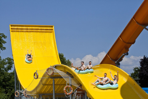 Young men riding inflatable rafts down a bright yellow waterslide at Camping Terme Catez in Slovenia.