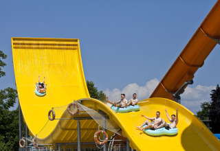 Young men riding inflatable rafts down a bright yellow waterslide at Camping Terme Catez in Slovenia.