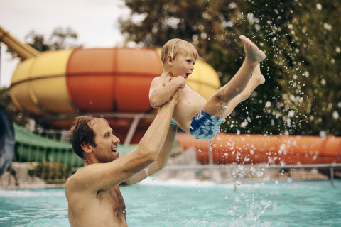Un hombre juega con un niño en la piscina de Camping Terme Catez, Eslovenia, con un tobogán de agua detrás.