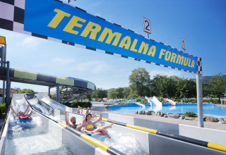 Persone si divertono sugli scivoli d'acqua sotto il cartello 'Termalna Formula' al Camping Terme Čatež, Slovenia.