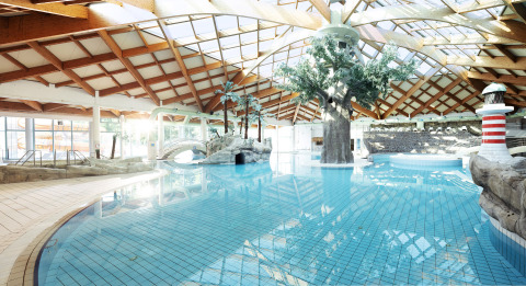 Indoor swimming pool with trees, bridge, and sunlight at Camping Terme Catez holiday park in Slovenia.