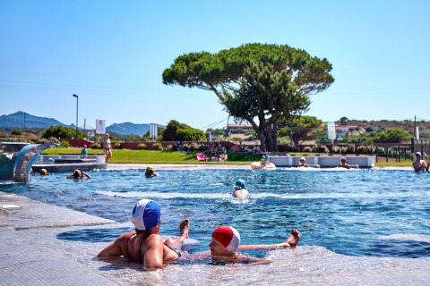 Personas disfrutan de la piscina en Camping Village Baia Blu La Tortuga, parque vacacional en Cerdeña, Italia.