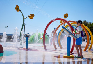 Children play on a colorful splash pad with water sprays at Camping Village Baia Blu La Tortuga, Sardinia, Italy.