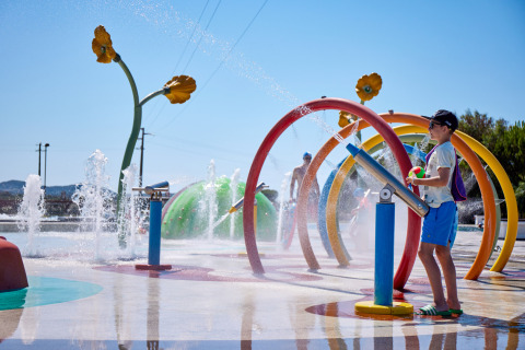 Children play on a colorful splash pad with water sprays at Camping Village Baia Blu La Tortuga, Sardinia, Italy.