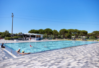 Udendørs swimmingpool i solskin med gæster, omkranset af træer på Camping Village Baia Blu La Tortuga, Sardinien.