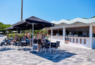 Outdoor snack bar with umbrellas and people relaxing at Camping Village Baia Blu La Tortuga in Sardinia, Italy.
