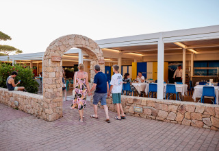 Ospiti passano sotto un arco di pietra all'ingresso del ristorante al Camping Village Baia Blu La Tortuga, Sardegna.