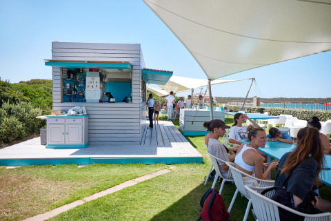 Outdoor dining area with guests and beach bar at Camping Village Baia Blu La Tortuga, Sardinia, Italy.