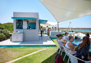Outdoor dining area with guests and beach bar at Camping Village Baia Blu La Tortuga, Sardinia, Italy.