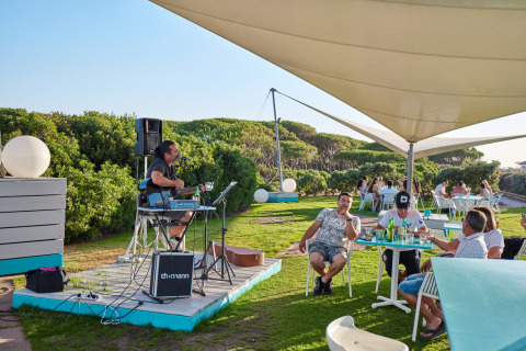 Café al aire libre en Camping Village Baia Blu La Tortuga en Cerdeña, con música en vivo y clientes disfrutando.