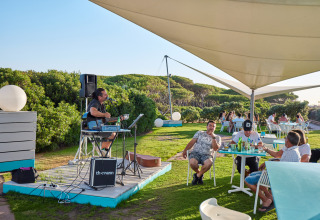 Udendørs café ved Camping Village Baia Blu La Tortuga i Sardinien med live musik og glade gæster.