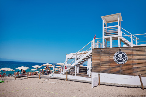 Beach scene at Camping Village Baia Blu La Tortuga in Sardinia with lifeguard tower and sun umbrellas.