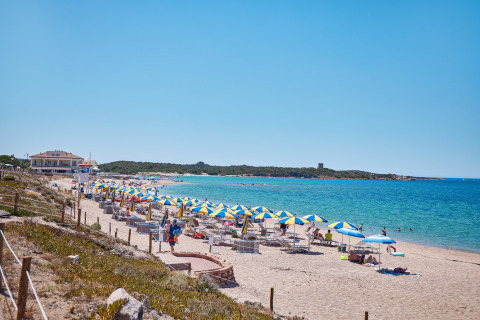 Spiaggia con ombrelloni blu e gialli al Camping Village Baia Blu La Tortuga in Sardegna, Italia, vicino al mare.
