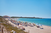 Strand med blå og gule parasoller på Camping Village Baia Blu La Tortuga i Sardinien, Italien, ved klart hav.