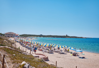 Strand med blå og gule parasoller på Camping Village Baia Blu La Tortuga i Sardinien, Italien, ved klart hav.