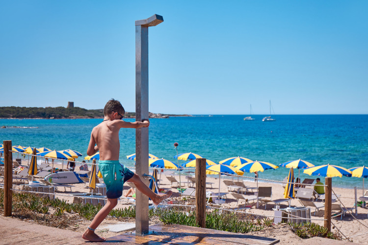 Garçon prenant une douche sur la plage à Camping Village Baia Blu La Tortuga, Sardaigne, Italie, avec parasols.