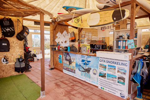 Tienda de equipos para deportes acuáticos en Camping Village Baia Blu La Tortuga en Cerdeña, con tablas y equipo de buceo.