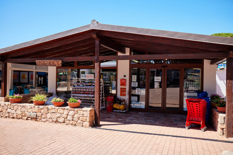 Entrance to a market at Camping Village Baia Blu La Tortuga, Sardinia, with plants and shopping carts outside.