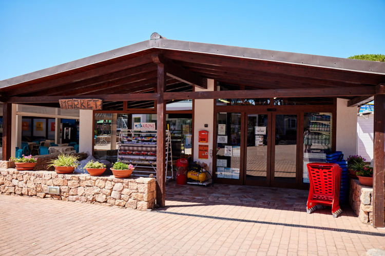 Entrée d’un marché au Camping Village Baia Blu La Tortuga, Sardaigne, avec des plantes et des chariots.