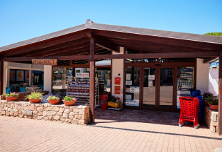 Ingresso del market al Camping Village Baia Blu La Tortuga, Sardegna, con piante e carrelli all’esterno.