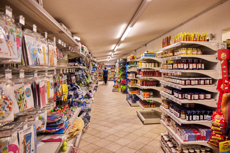 Allée dans une supérette du Camping Village Baia Blu La Tortuga avec rayons remplis de produits variés.
