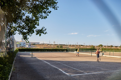 Due persone giocano a tennis su un campo all'aperto sotto il cielo azzurro al Camping Village Baia Blu La Tortuga, Sardegna.