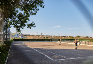 Due persone giocano a tennis su un campo all'aperto sotto il cielo azzurro al Camping Village Baia Blu La Tortuga, Sardegna.