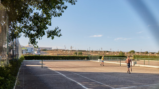 Dos personas juegan al tenis en una pista al aire libre bajo el cielo azul en Camping Village Baia Blu La Tortuga, Cerdeña.
