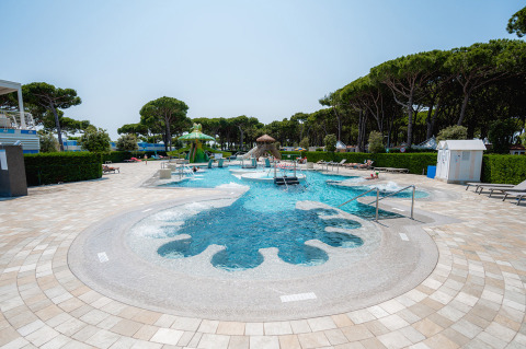 Piscina exterior con tumbonas y árboles en Camping Village Cavallino, parque vacacional en Véneto, Italia.